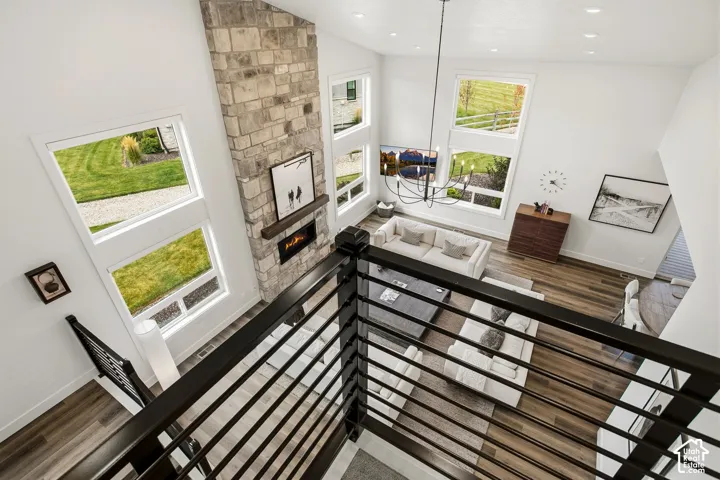 Two-story stone-clad fireplace with mantel, multi-level window arrangement, wood-finish flooring, metal railing, and recessed lighting
