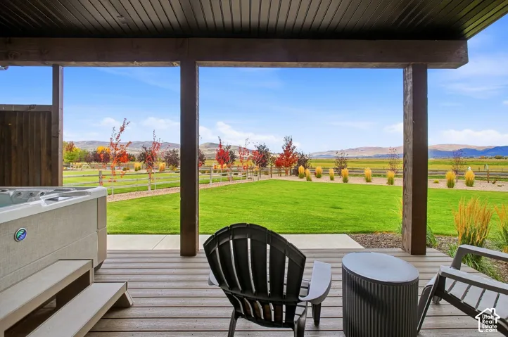 Covered outdoor living area, wood-finish deck flooring, built-in spa, expansive manicured lawn, and mature trees