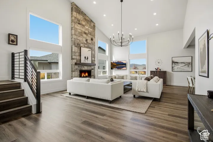 Vaulted ceilings with recessed lighting, large windows, wood-finish flooring, stone-clad fireplace with mantel, and a black wrought iron staircase railing