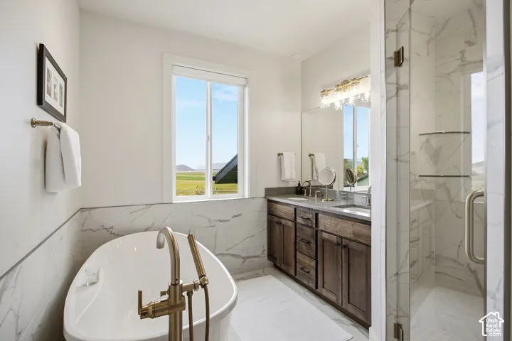 Freestanding soaking tub with a brushed bronze floor-mounted faucet, dual vanity with a dark wood-finish cabinet, and a glass-enclosed shower with full-height tile surround