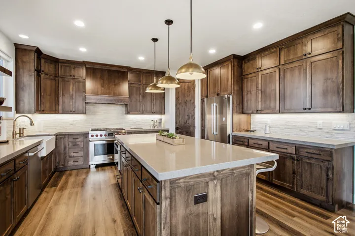 Kitchen featuring wood-finish flooring, custom wood cabinetry, stainless steel appliances, a large center island with seating, and pendant lighting