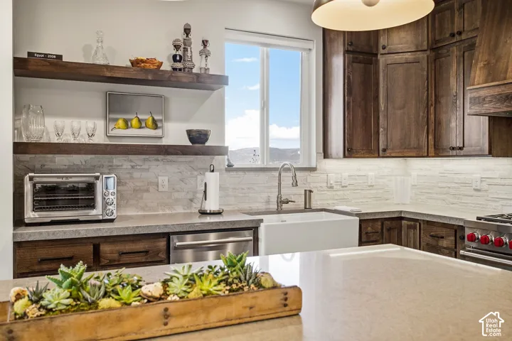 Kitchen featuring dark wood cabinetry, white farmhouse sink, light stone countertops, and textured tile backsplash