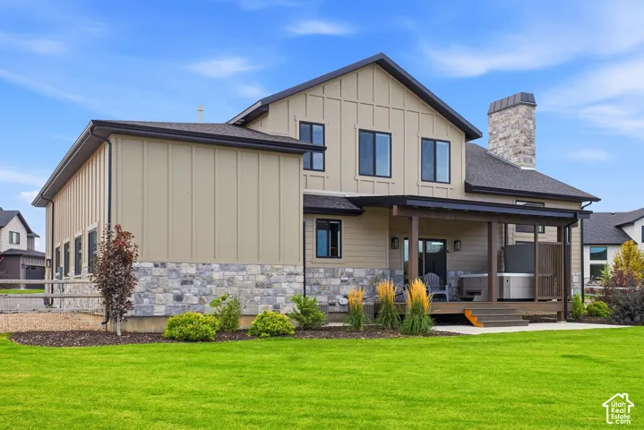 Expansive green lawn, a covered patio, stone and board-and-batten siding, a stone-clad chimney, and black-framed windows