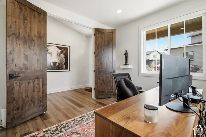 Angled vaulted ceiling, wood-finish flooring, dark wood double doors, white window trim, and recessed lighting