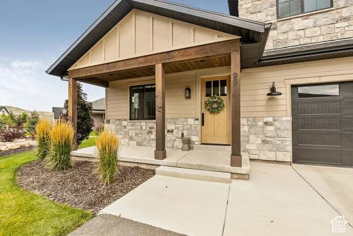 Welcoming front porch featuring a gabled roof with exposed wood beams, stone and siding exterior, wooden entry door with transom window, and integrated sconce lighting