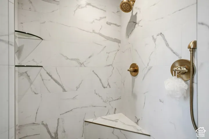 Shower with large format tile, brass fixtures, a rain showerhead, and a built-in bench