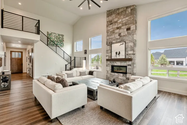 Vaulted ceiling with a contemporary ceiling fan, stone-clad fireplace with a wood mantel, wood-finish flooring, staircase with black horizontal railings, and a multi-pane glass entry door