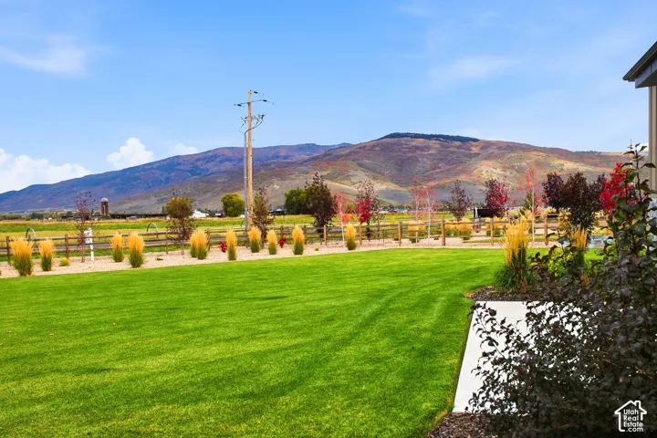 Manicured lawn with mature landscaping, wood fence, distant mountain range, and clear skies