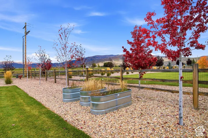 Expansive outdoor area featuring a split-rail fence, gravel landscaping, manicured lawn, and mature trees