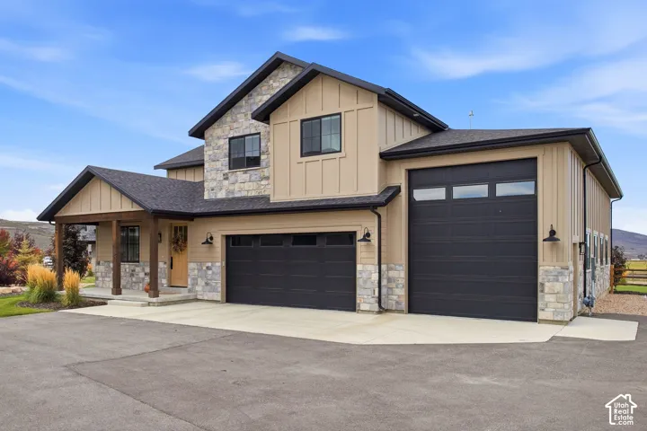 Exterior featuring board and batten siding, stone accents, dark-framed windows, and multiple dark garage doors