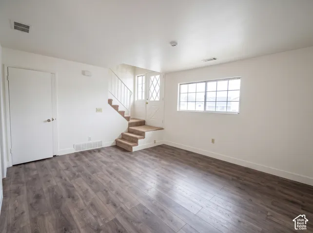 Interior space featuring wood-finish flooring, a carpeted staircase with white metal railings, a multi-pane glass door, and a single-hung window with a grid pattern