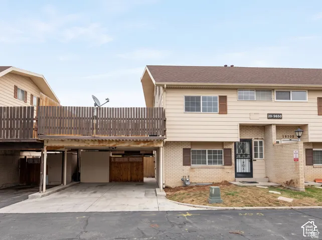 Multi-level exterior featuring light-toned brick and horizontal siding, covered carport, and second-story wood-slat balcony