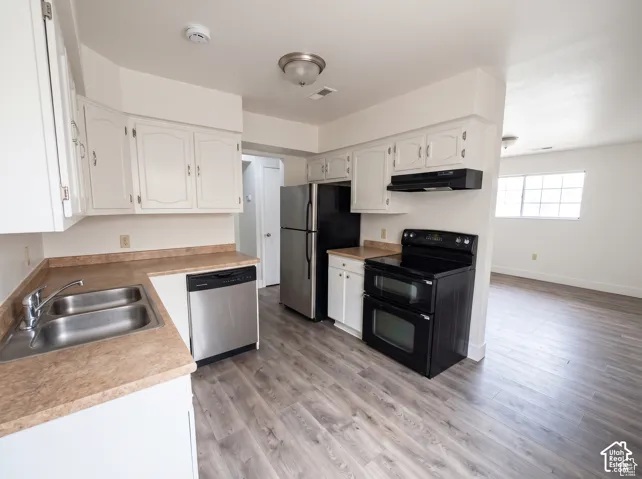 Kitchen featuring white cabinetry, wood-finish flooring, laminate countertops, stainless steel dishwasher, and black double oven range