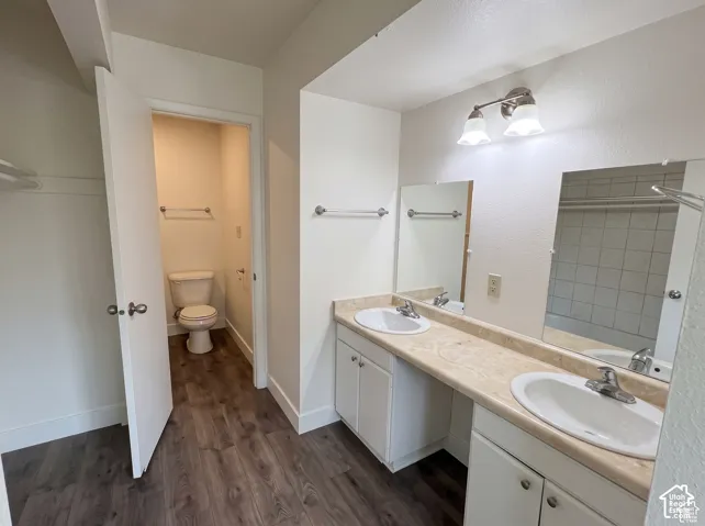 Dual-sink vanity with stone-finish countertop, wood-finish flooring, dual wall-mounted mirrors, and two-light vanity fixture
