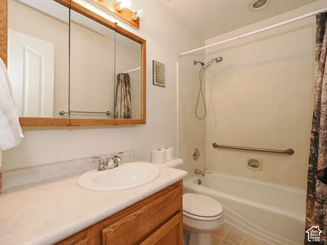 Bathroom featuring wood-tone cabinetry, integrated countertop with inset sink, three-panel medicine cabinet, and a shower-tub combination with a wall-mounted grab bar