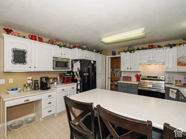 Kitchen featuring white cabinetry, integrated desk space, solid surface countertops, and stainless steel appliances