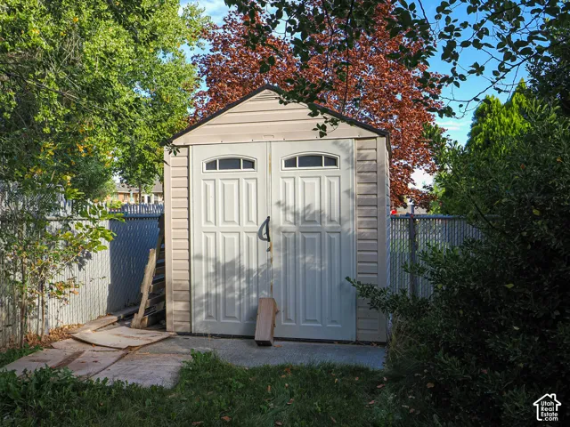 Detached storage shed featuring double doors with arched windows, gable roof, and textured siding