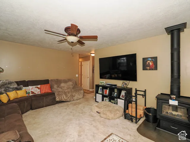 Living area featuring a freestanding wood-burning stove with a matte black metal flue, wall-to-wall carpeting, and a ceiling-mounted fan with integrated lighting
