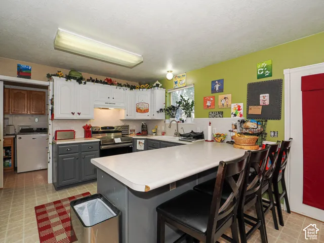 Kitchen featuring two-tone cabinetry, stainless steel range, peninsula with overhang, and a dual-basin sink with a gooseneck faucet