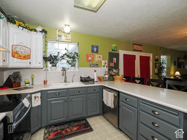 Kitchen featuring grey lower cabinetry, white upper cabinetry, white countertops, stainless steel appliances, and a double-basin sink