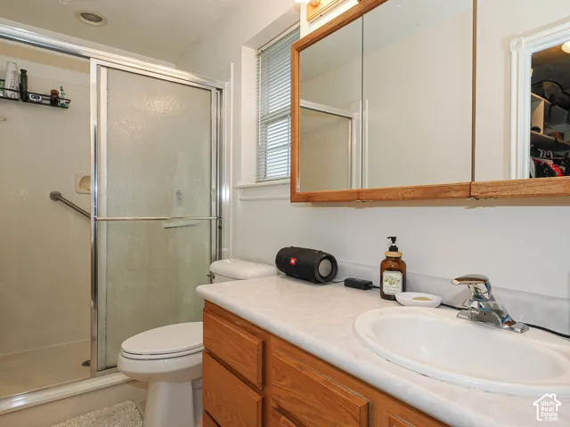 Bathroom featuring a wooden vanity with a stone-finish countertop, oval undermount sink, built-in wooden medicine cabinet, and a walk-in shower with a sliding glass door and chrome-finish hardware