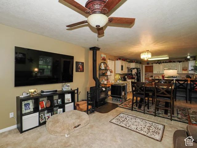 Open-concept space featuring a wood-burning stove, ceiling fan with integrated lighting, and kitchen cabinetry