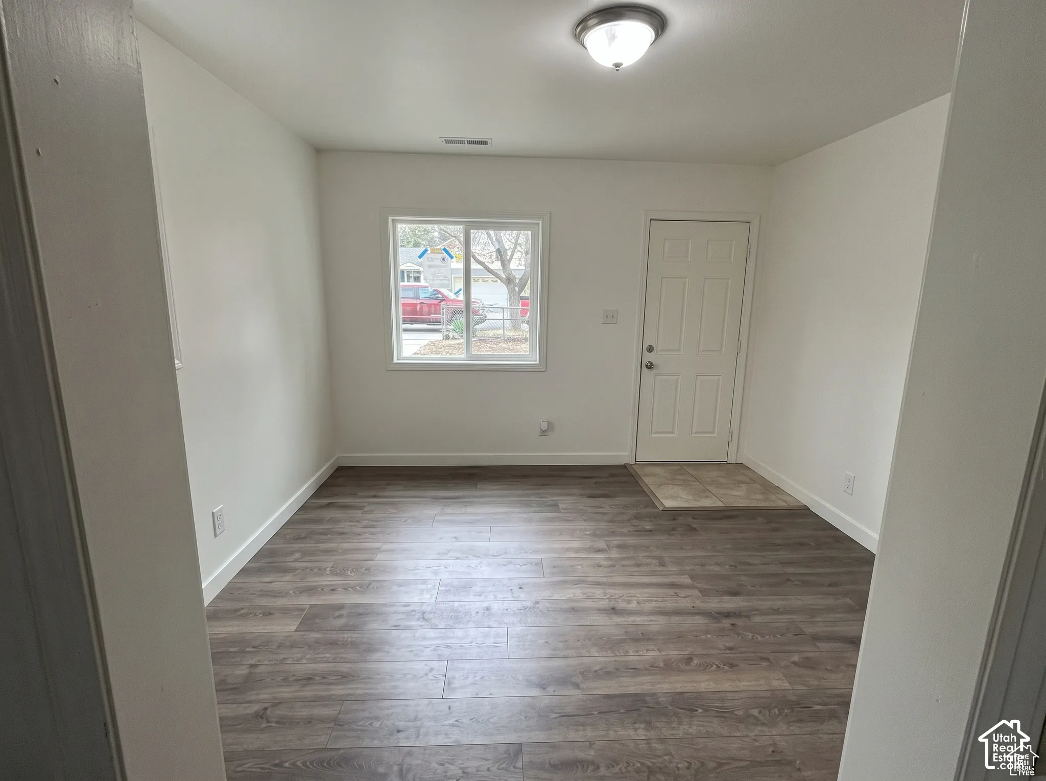 Interior space featuring wood-finish flooring, neutral wall tones, a sliding window, a flush-mount ceiling light fixture, and a tiled entry area