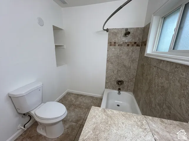 Bathroom featuring large-format tile flooring, a porcelain tub with a decorative tile surround, a curved shower rod, and built-in wall shelving