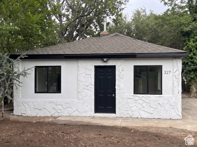 Exterior facade featuring textured white masonry, contrasting black window frames, a dark-toned entry door, and a shingled hipped roof