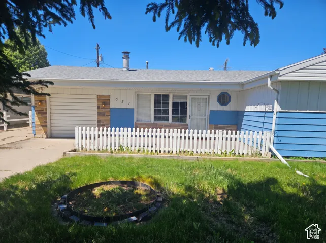 Single-story exterior featuring a mix of horizontal siding and stone masonry, a white picket fence, a concrete driveway, and an integrated garage