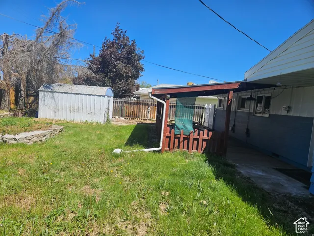 Backyard space featuring a covered patio, a detached metal storage shed, and a stone-bordered garden area enclosed by wood and vinyl fencing