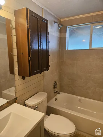 Bathroom featuring large-format wall tile, built-in wooden cabinetry, a rectangular sink with integrated countertop, and a shower-tub combination with chrome fixtures
