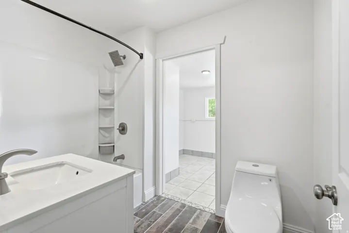 Bathroom featuring a single-sink vanity with a solid-surface countertop, a tub-shower combination with an integrated multi-tier shelf, a rainfall showerhead, and wood-finish flooring