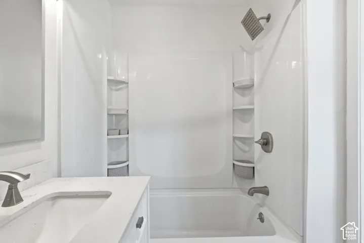 Bathroom featuring a white vanity with a stone countertop, an integrated rectangular sink, a bathtub and shower combination with built-in shelving, and brushed nickel hardware