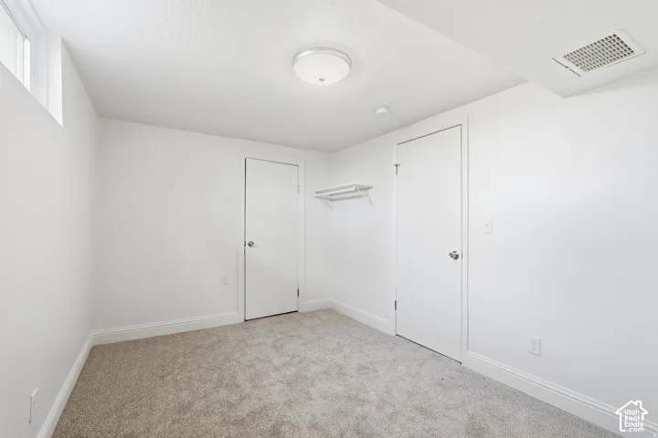Room featuring neutral-toned carpeting, two interior doors, a wall-mounted shelving unit, and a ceiling-mounted light fixture