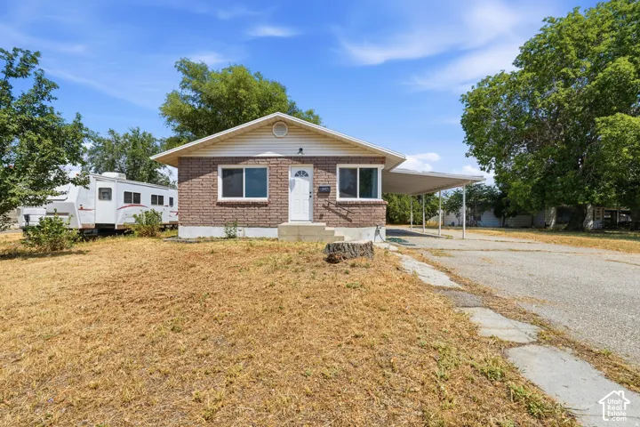 Single-story brick exterior featuring a gable roof, concrete steps, and an attached carport with a paved driveway