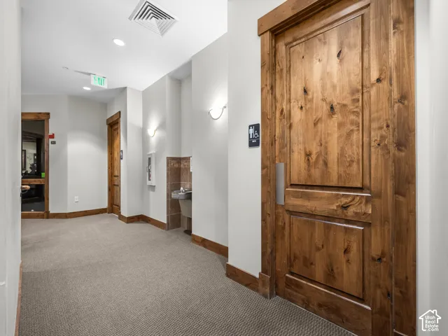 Hallway featuring solid wood-cased doors, neutral wall-to-wall carpeting, wall-mounted sconce lighting, and a recessed water fountain with stone tile surround