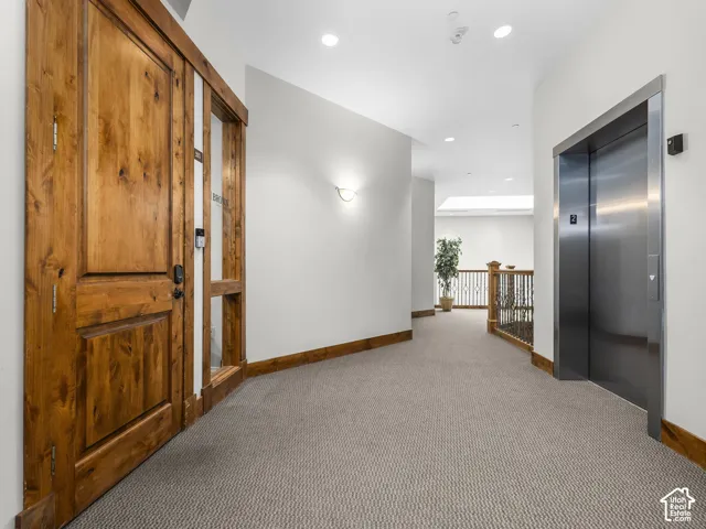 Solid knotty wood door with glass sidelight, stainless steel elevator, recessed lighting, and ornate metal stair railing