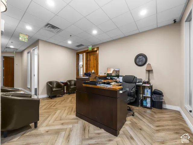 Reception area featuring herringbone wood-finish flooring, recessed ceiling lighting, drop-ceiling panels, and natural wood-trim door frames