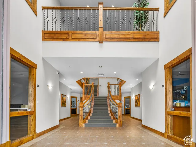 Double-height foyer featuring a central carpeted staircase with decorative wooden railings, tile flooring, interior glass-paneled entryways, and custom wood trim detailing