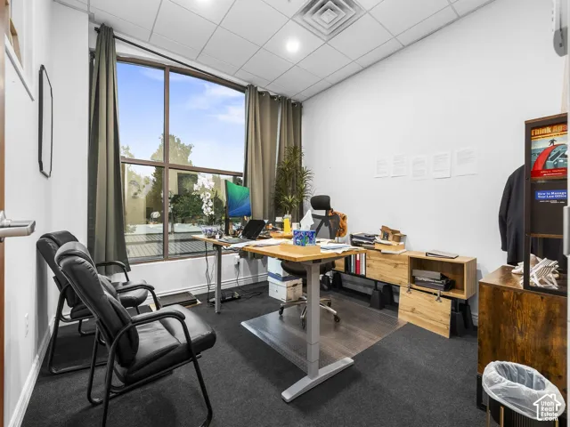 Office space featuring floor-to-ceiling windows, grid-style drop ceiling, and dark carpeting