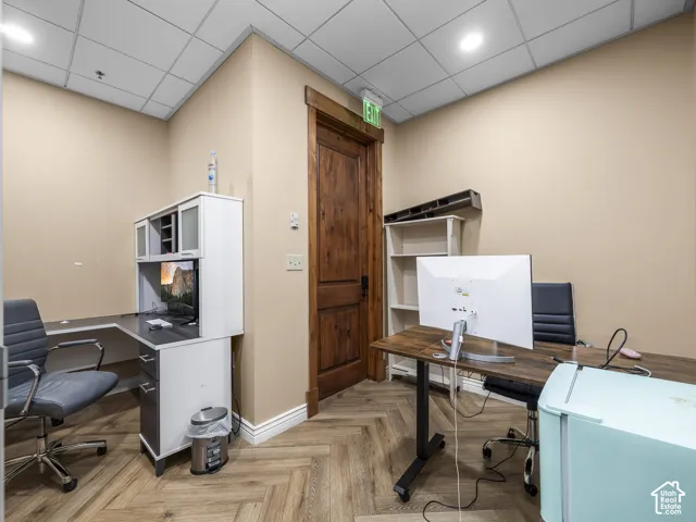 Wood-finish flooring in a herringbone pattern, stained wood interior door with matching trim, recessed lighting, and drop ceiling tiles