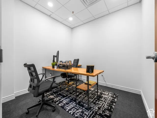 Enclosed room featuring neutral wall paint, dark carpeting, and a drop ceiling with recessed lighting