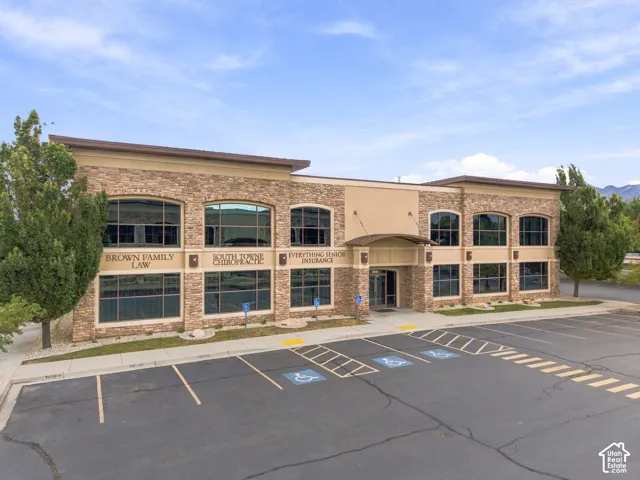 Two-story commercial building featuring a stone veneer exterior, expansive glass window panels, a covered entry, and a paved parking area