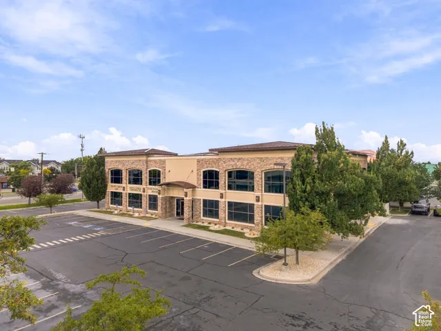 Two-story commercial exterior featuring stone veneer siding, expansive glass windows, paved surface parking, and mature landscaping