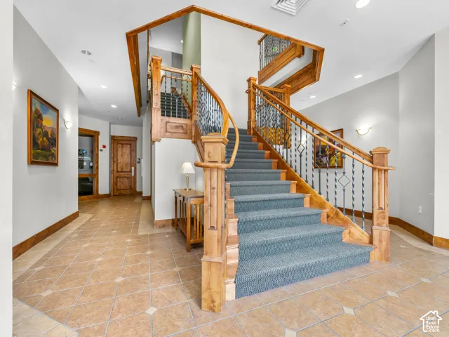 Grand foyer featuring tile flooring with decorative inserts, a staircase with custom wood handrails, ornamental metal balusters, and solid wood-trim door frames
