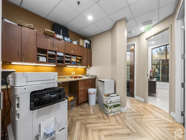 Workspace featuring custom wood-finish cabinetry, under-cabinet lighting, a built-in laminate desk surface, and wood-finish herringbone flooring
