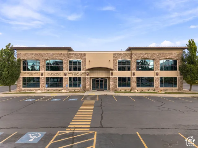 Two-story commercial building featuring stacked stone masonry, a flat roofline, extensive glass window arrays, and an asphalt parking lot