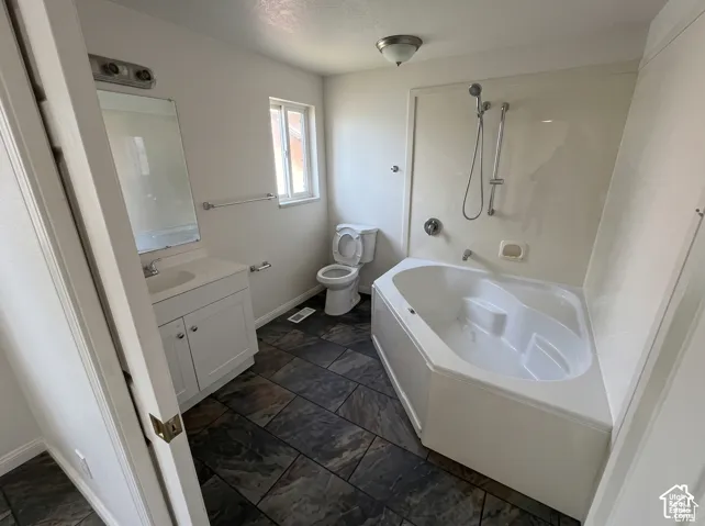Bathroom featuring large-format slate-finish tile flooring, a soaking tub with integrated shower hardware, white cabinetry with a light-tone countertop, and a wall-mounted mirror