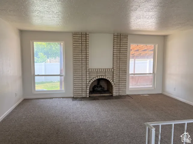 Floor-to-ceiling brick fireplace with arched hearth, neutral carpeting, and dual oversized windows